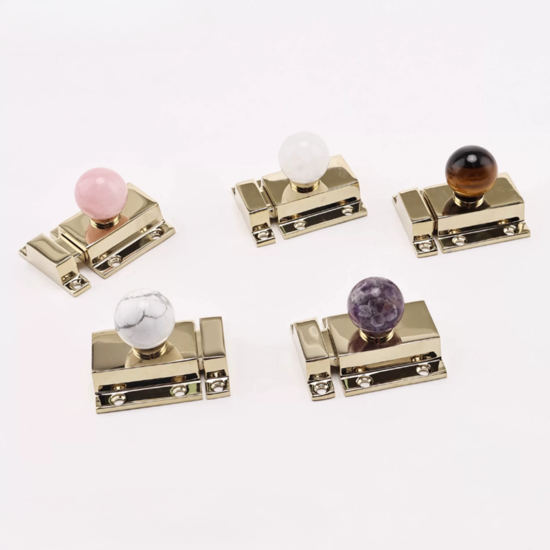 Five gold-toned cabinet knobs with round marble-style accents in pink, white, brown, white, and purple, arranged on a clean white background.