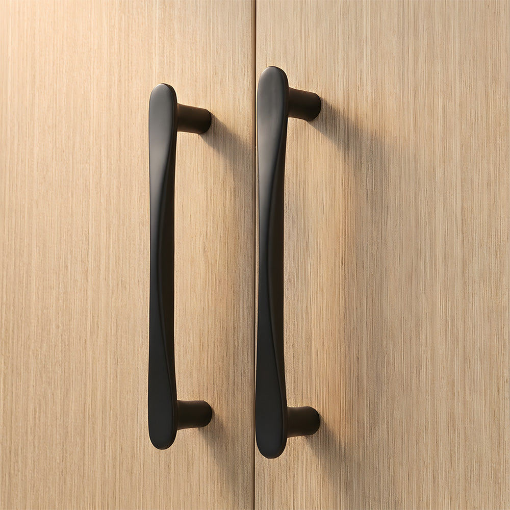 Black tapered arched brass cabinet pull, shown at close range in an installed cabinet close-up