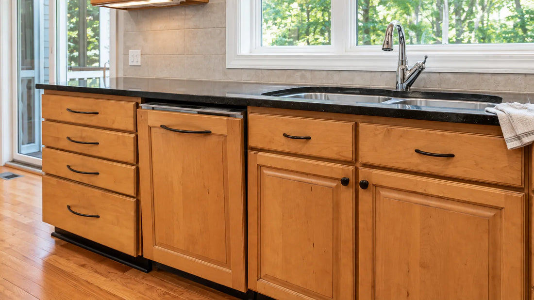 Panel-ready dishwasher with matching black cabinet pulls installed on natural wood kitchen cabinets