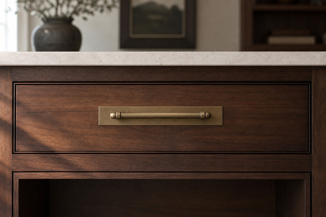 Antique brass cabinet pull with a rectangular backplate on a dark wood drawer