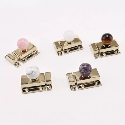 Five gold-toned cabinet knobs with round marble-style accents in pink, white, brown, white, and purple, arranged on a clean white background.