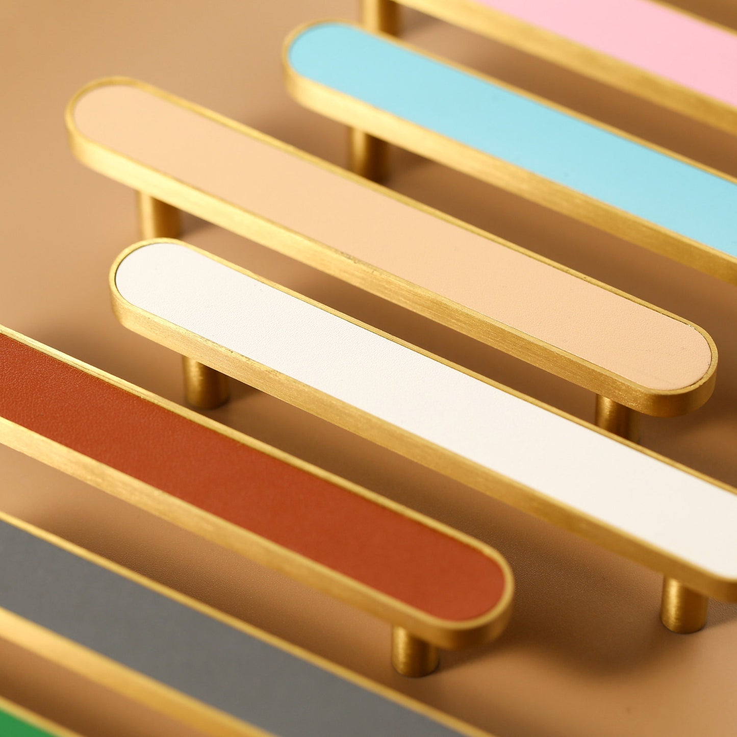 Gold-tone leather-inlay cabinet pulls in multiple colors arranged diagonally on a warm background
