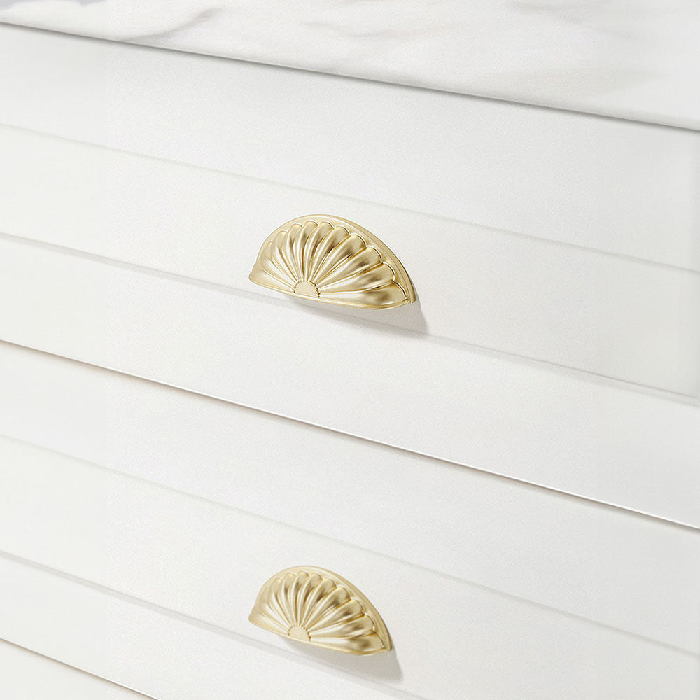 Gold shell-shaped cabinet cup pull, shown at close range installed on cabinetry in context