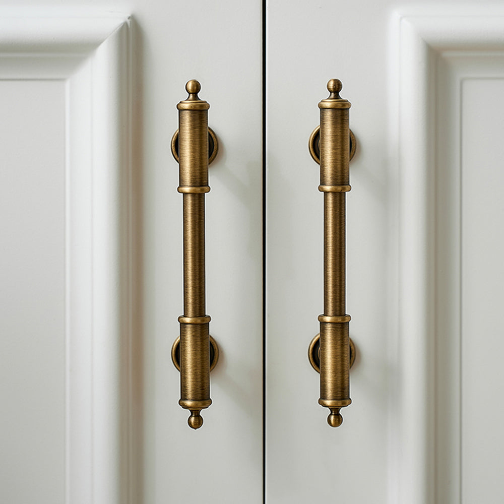 Antique brass round bar cabinet pull with matching T-knob, shown in a focused view in an installed cabinet close-up