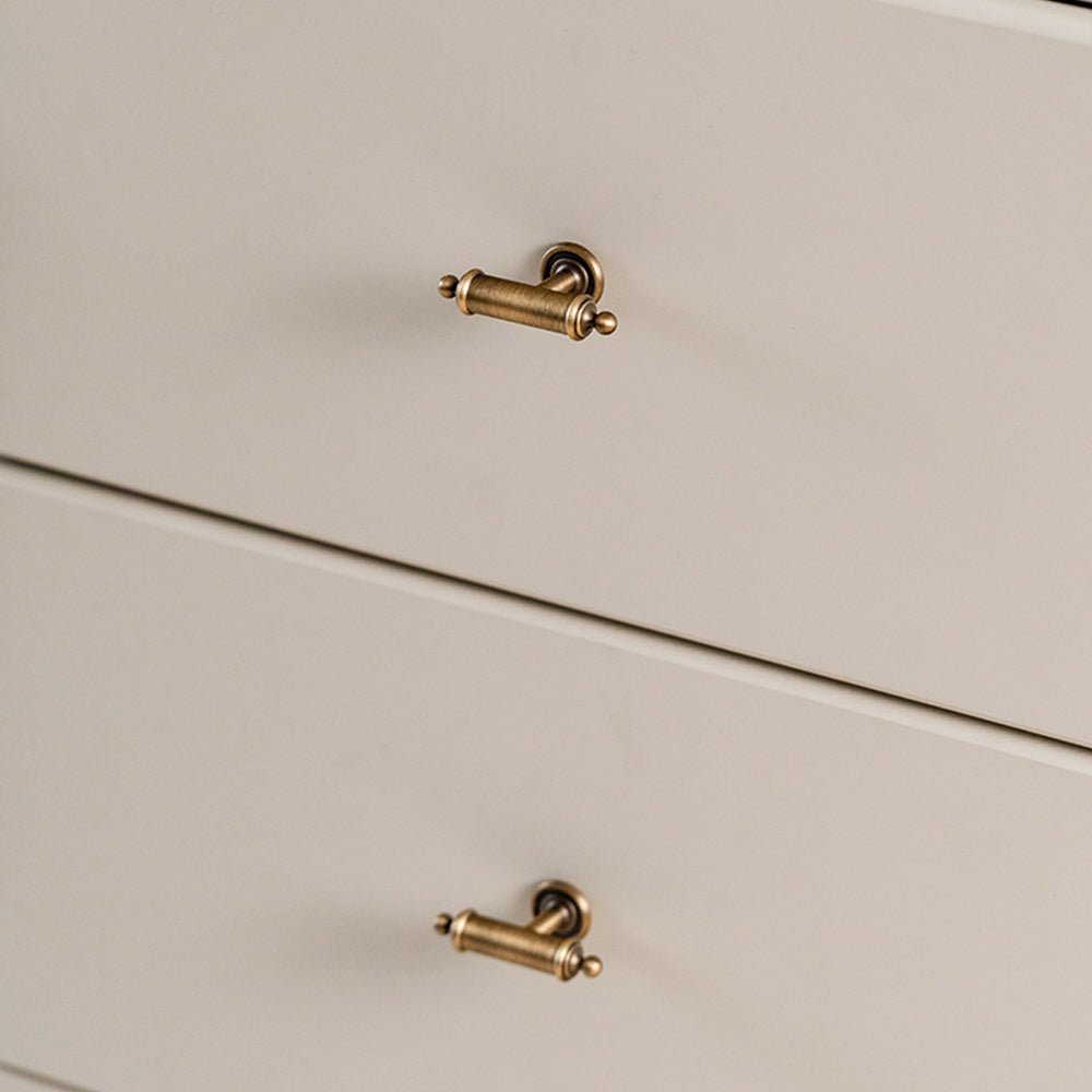 Antique brass round bar cabinet pull with matching T-knob, shown at close range installed on cabinetry in context