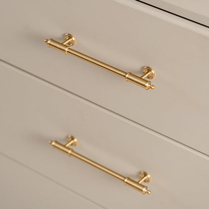 Antique brass round bar cabinet pull with matching T-knob, shown from one angle installed on cabinetry in context