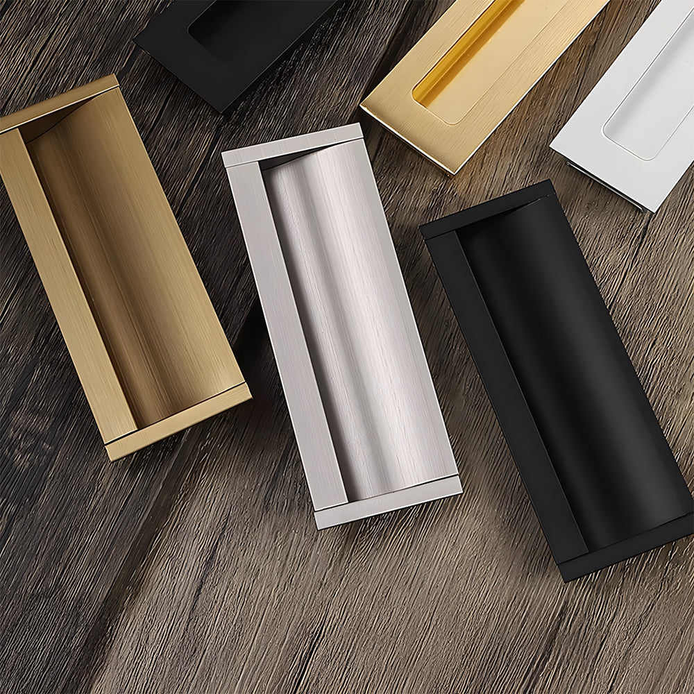Gold, silver, black, white, and bronze recessed cabinet pulls arranged on a wood surface