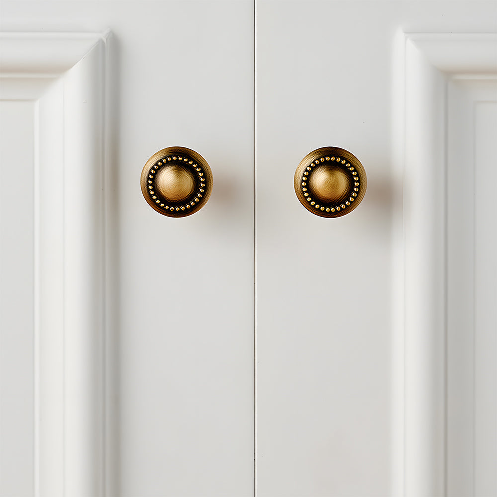 Ornate european brass cabinet pull and round knobs, shown in a focused view installed on cabinetry in context