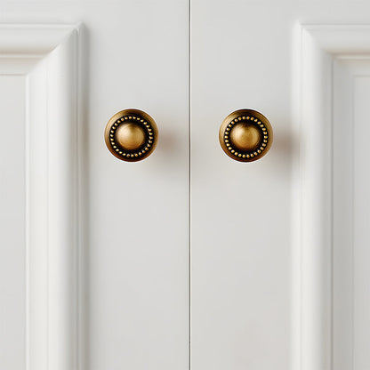Ornate european brass cabinet pull and round knobs, shown in a focused view installed on cabinetry in context