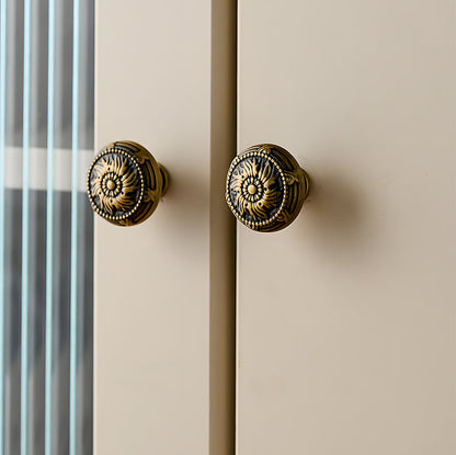 Ornate european brass cabinet pull and round knobs, shown from one angle mounted on a finished cabinet front