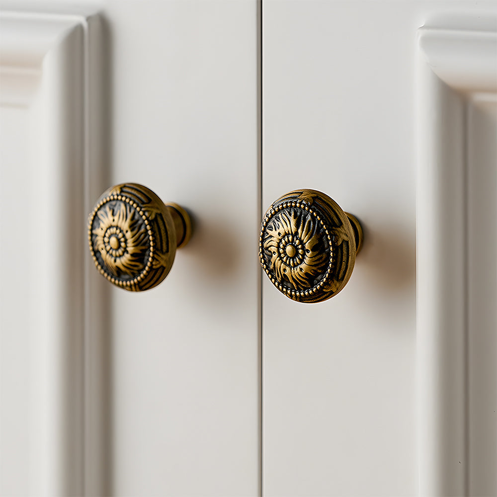 Ornate european brass cabinet pull and round knobs, shown at close range installed on cabinetry in context