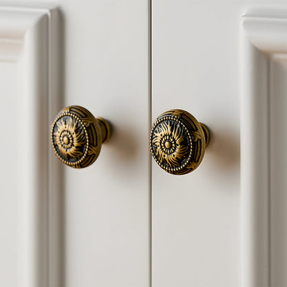 Ornate european brass cabinet pull and round knobs, shown at close range installed on cabinetry in context