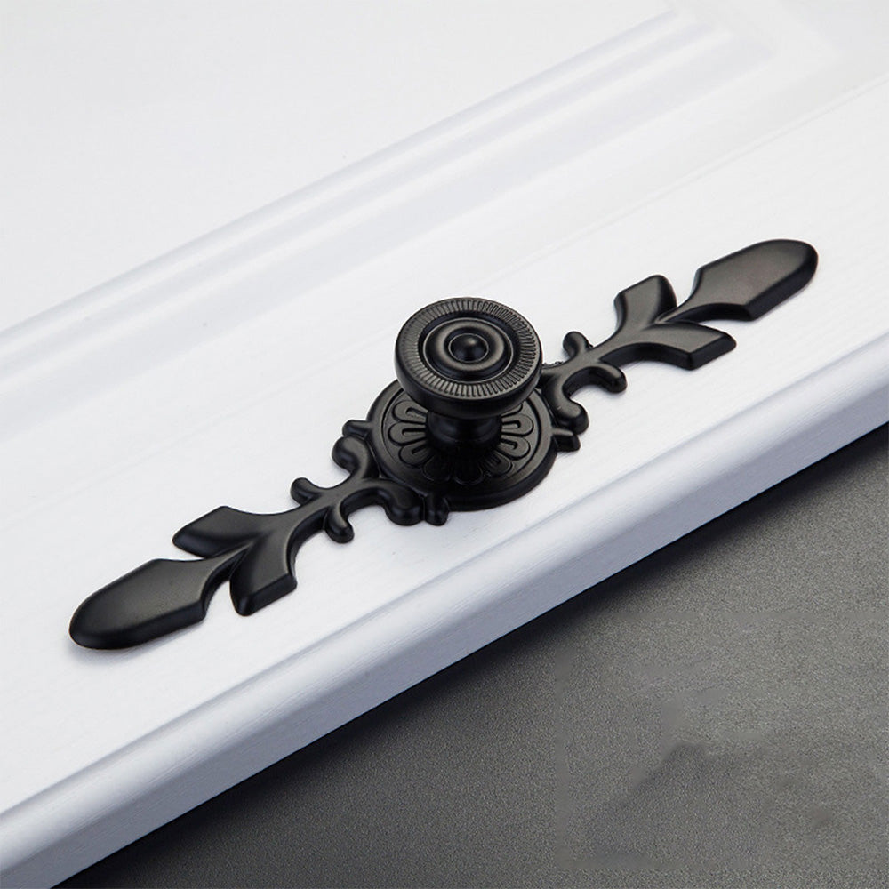 Black round cabinet knob with ornate floral backplate, shown from one angle on a clean neutral background