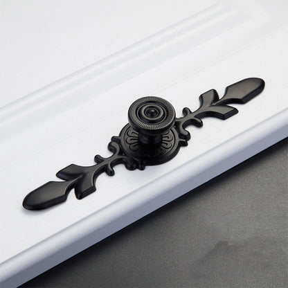 Black round cabinet knob with ornate floral backplate, shown from one angle on a clean neutral background