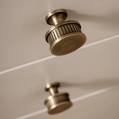 Ribbed bronze cabinet pull and round knob, presented for reference in an installed cabinet close-up