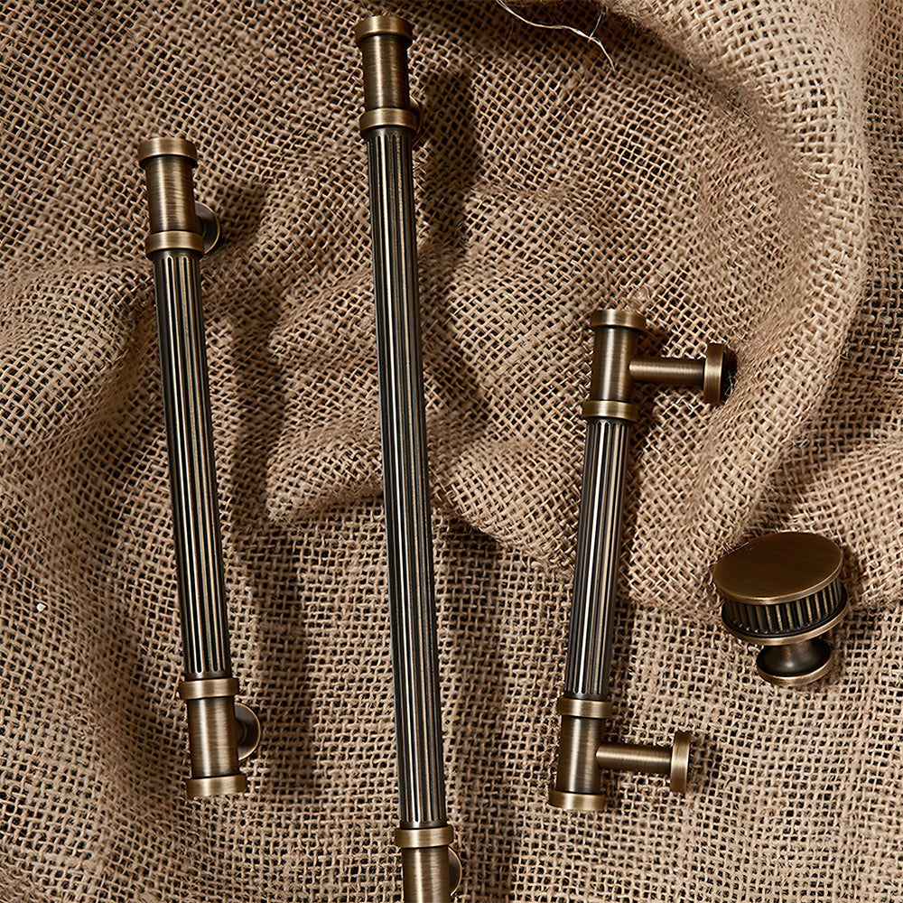 Ribbed bronze cabinet pull and round knob, shown from one angle with related hardware in one display