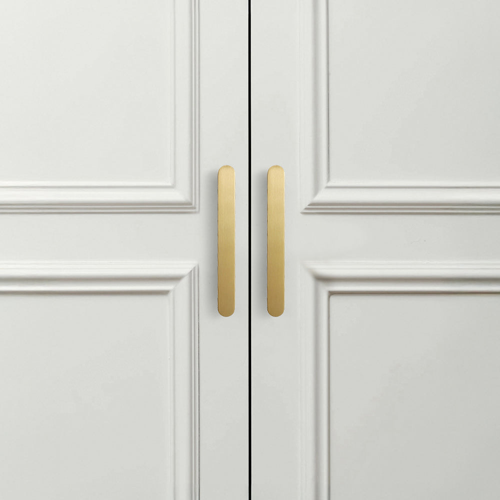 Gold rounded-edge brass cabinet pull and round knob, shown from one angle in an installed cabinet close-up