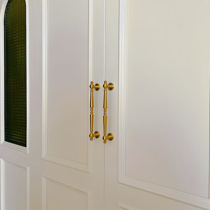 Vintage turned brass cabinet pull and round knob, shown from one angle mounted on a finished cabinet front