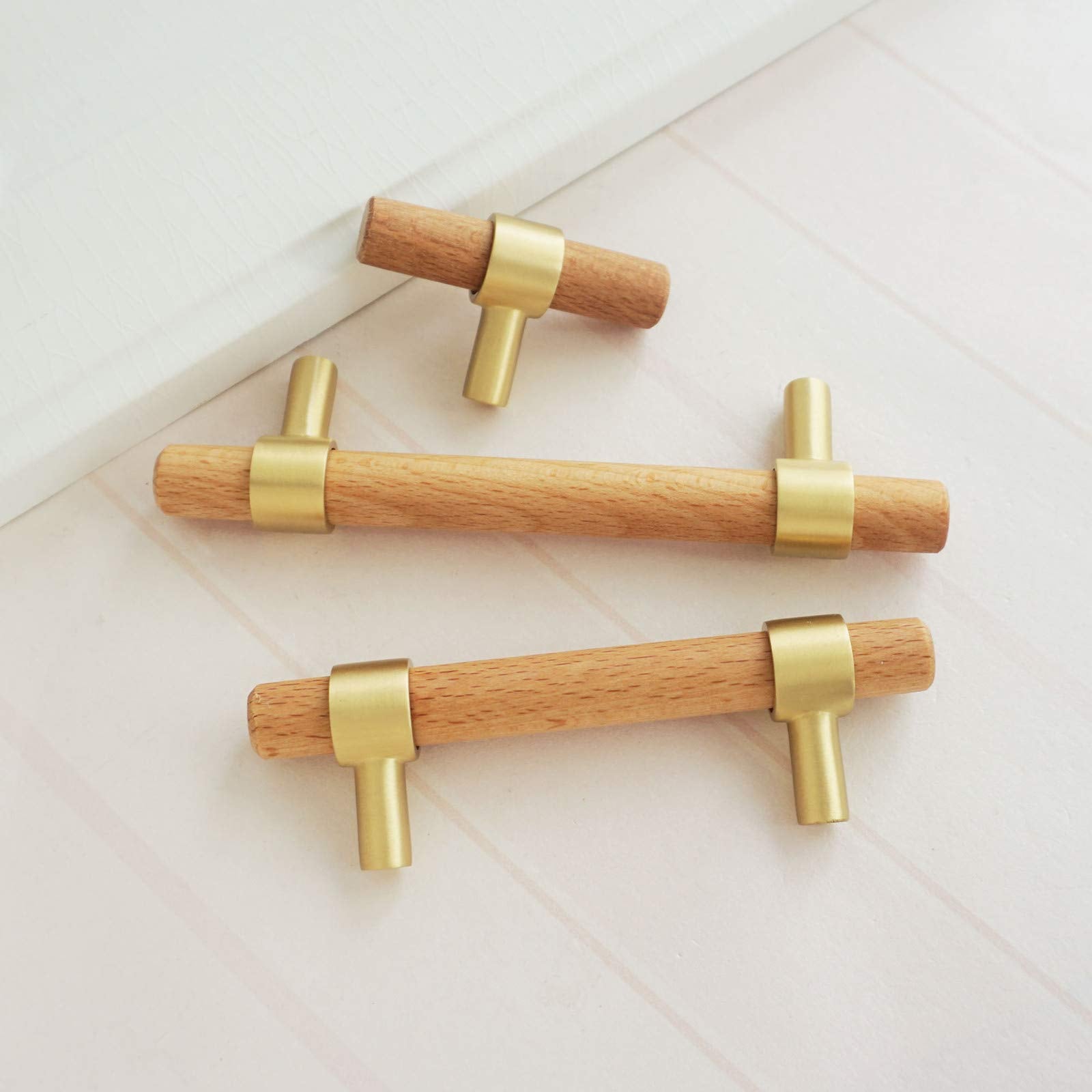 Walnut or beech wood cabinet pull with brushed brass bases, grouped in long and short versions on a neutral surface