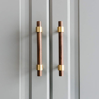 Walnut or beech wood cabinet pull with brushed brass bases, installed on paired cabinet doors in a close view