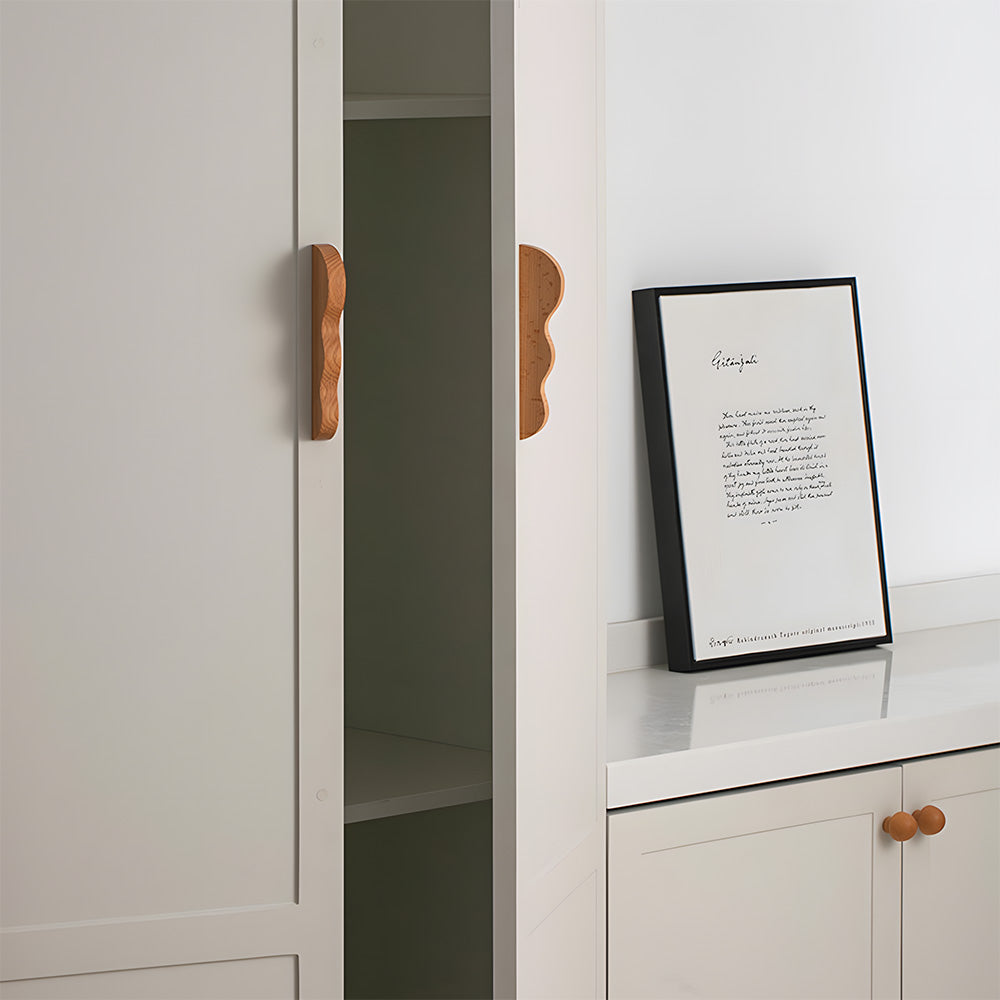 Wavy wood cabinet pull with a sculpted three-curve profile, installed on light cabinet doors with the profile visible