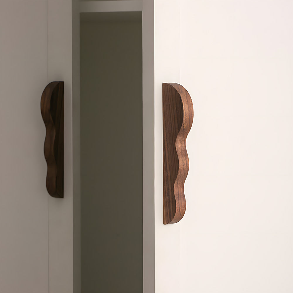 Wavy wood cabinet pull with a sculpted three-curve profile, mounted on tall cabinet doors in a wider room view
