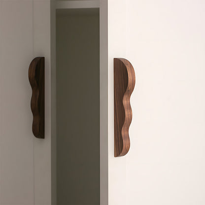 Wavy wood cabinet pull with a sculpted three-curve profile, mounted on tall cabinet doors in a wider room view