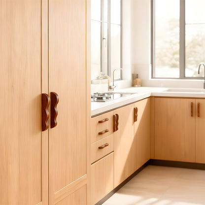 Wavy wood cabinet pull with a sculpted three-curve profile, installed on kitchen cabinet doors and drawers