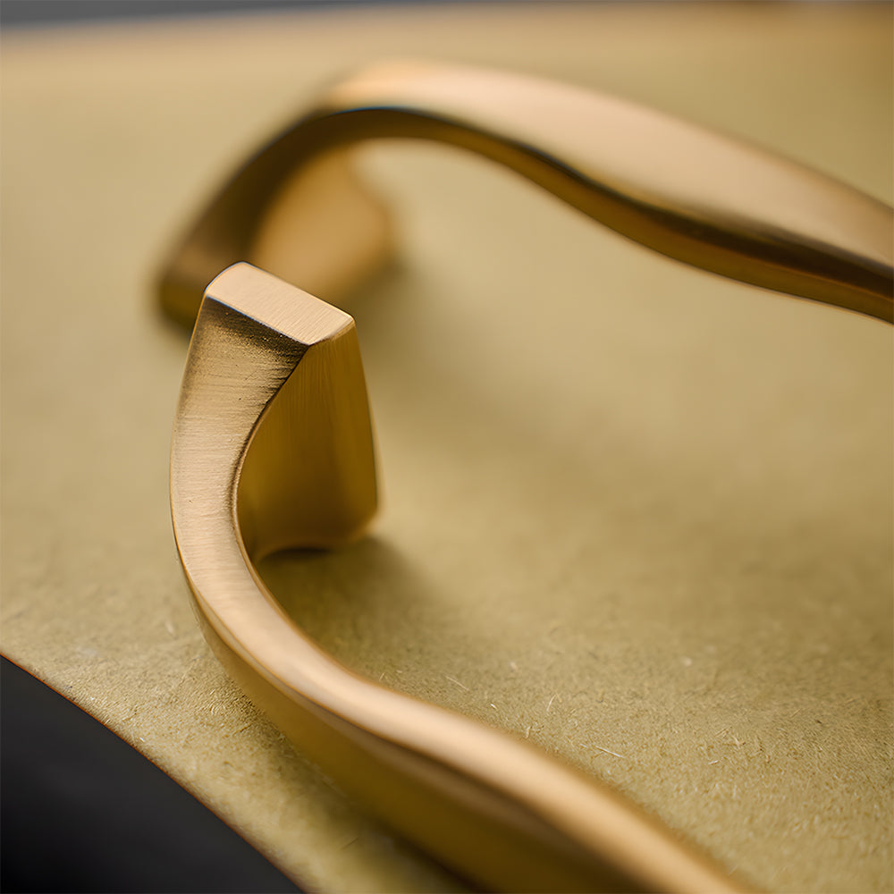 Wide arched brass cabinet pull with flared square ends, pictured in one view in an installed cabinet close-up