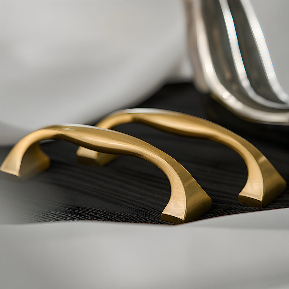 Wide arched brass cabinet pull with flared square ends, displayed from the side as a color and finish lineup