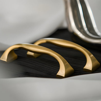 Wide arched brass cabinet pull with flared square ends, displayed from the side as a color and finish lineup