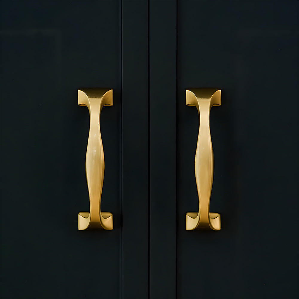 Wide arched brass cabinet pull with flared square ends, displayed from the side installed on cabinetry in context
