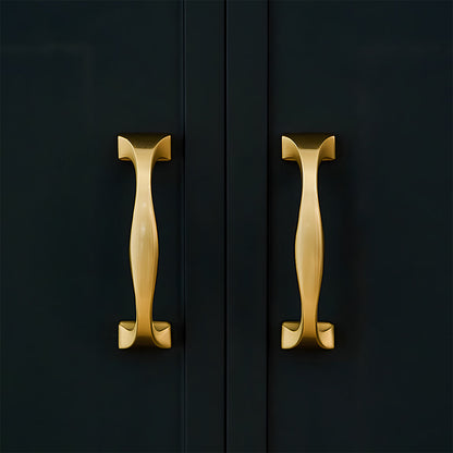 Wide arched brass cabinet pull with flared square ends, displayed from the side installed on cabinetry in context