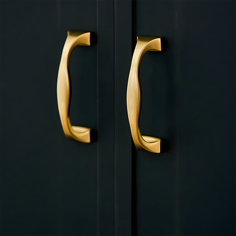 Wide arched brass cabinet pull with flared square ends, presented in another view installed on cabinetry in context