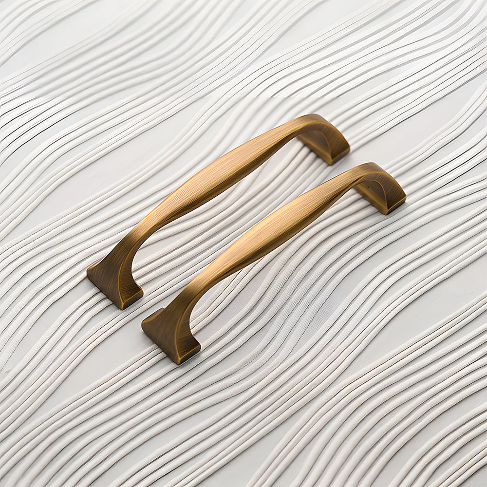 Wide arched brass cabinet pull with flared square ends, shown from one angle as a color and finish lineup