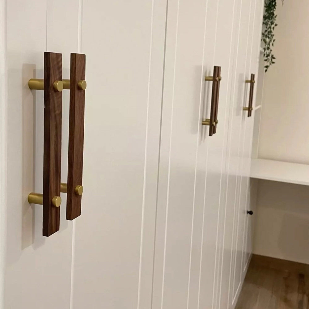 Wood-grain cabinet pull with metal posts in light wood with gold posts, installed vertically on paired wardrobe doors