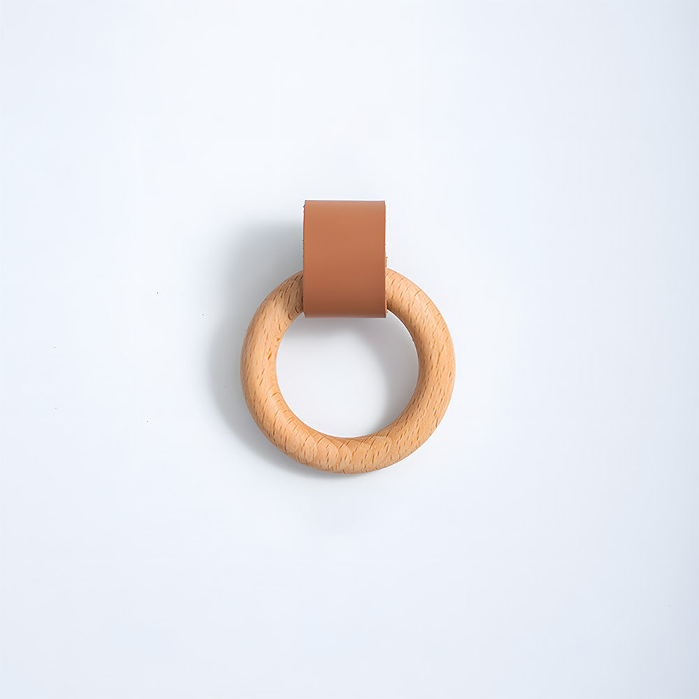 Wood ring cabinet knob with a brown leather strap in a slightly angled front view on white