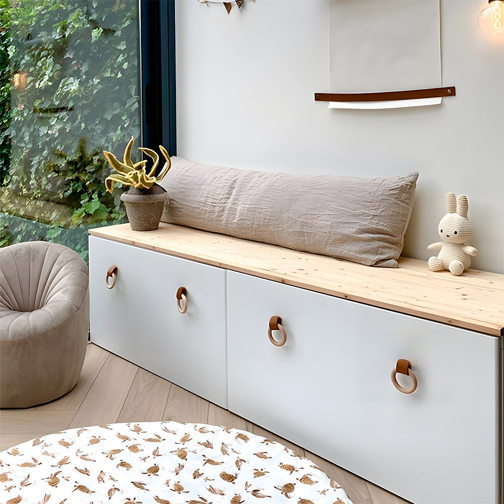 Wood ring cabinet knobs with leather straps installed on white storage bench doors in a bright room