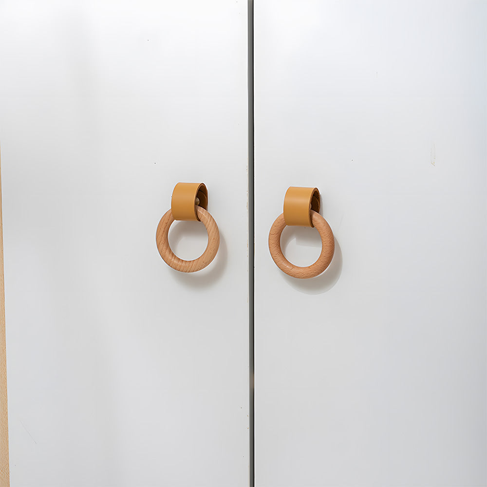 Two wood ring cabinet knobs with caramel leather straps on paired white cabinet doors