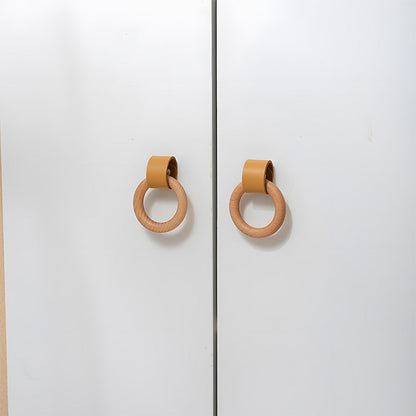 Two wood ring cabinet knobs with caramel leather straps on paired white cabinet doors