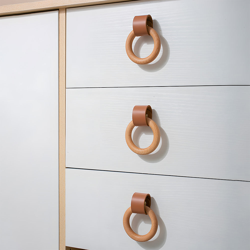 Three caramel leather and wood ring cabinet knobs installed on stacked white drawer fronts