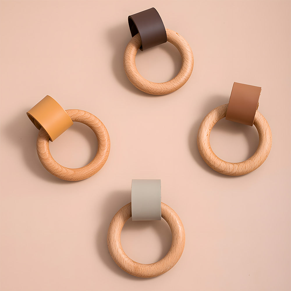 Four wood ring cabinet knobs showing multiple leather strap color options on a pink surface