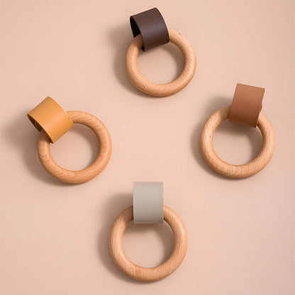Four wood ring cabinet knobs showing multiple leather strap color options on a pink surface
