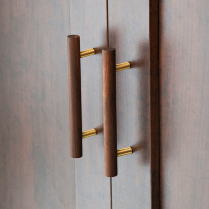 Wood cabinet pull with brass posts in brown with 96 mm centers, mounted on tall cabinet doors in a wider room view