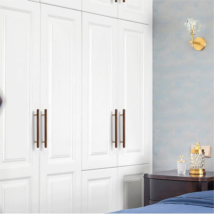 Wood and brass cabinet pull with a round bar profile, installed vertically on paired wardrobe doors