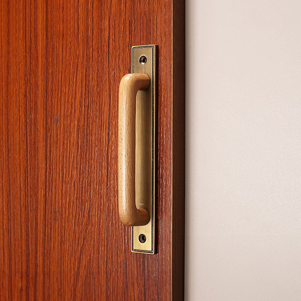 Wood cabinet pull with a rectangular metal backplate, shown from one angle installed on cabinetry in context