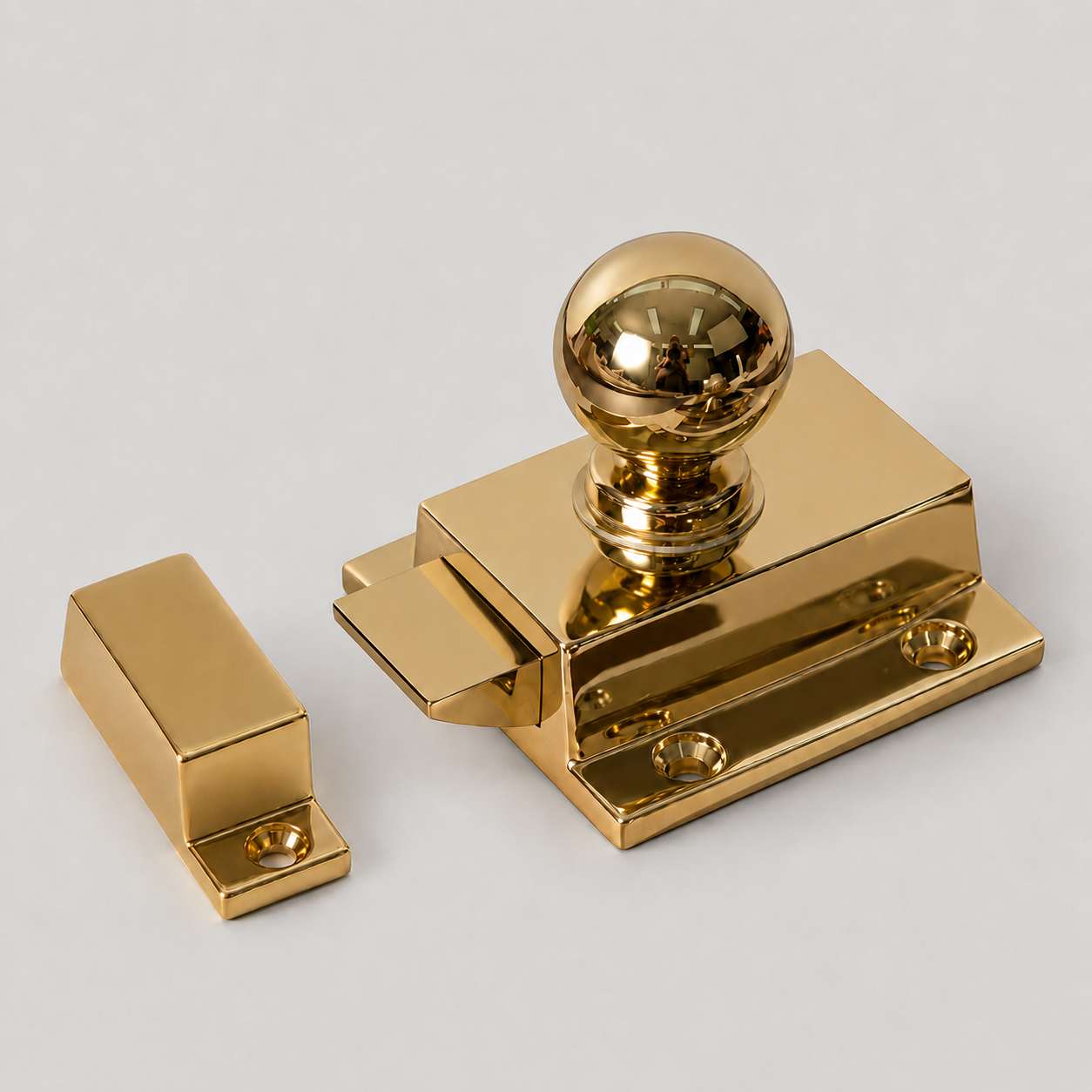 A polished gold metal ball latch and matching strike piece on a light gray background.